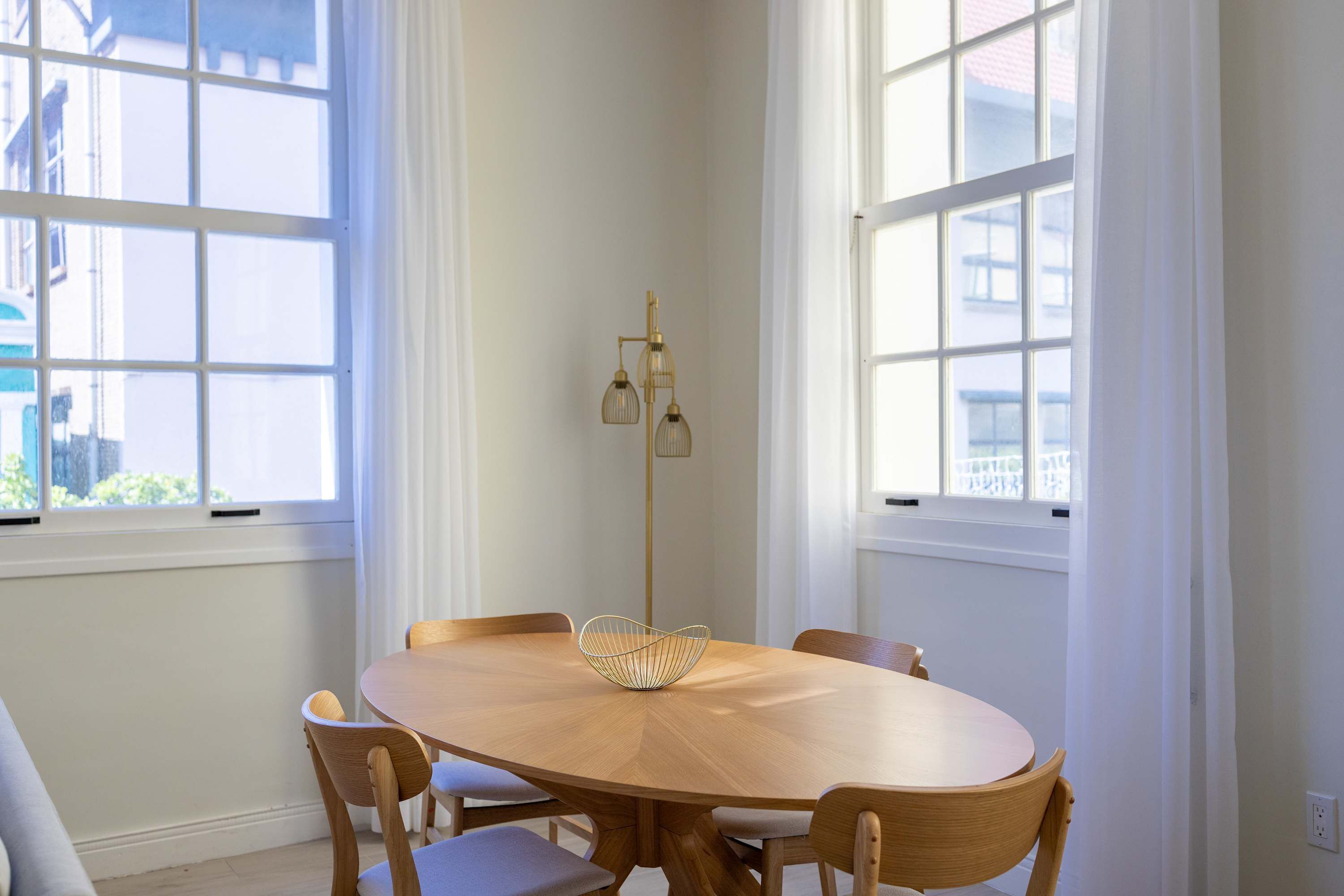 A dining area with a wooden oval table, four chairs, a woven bowl, and a floor lamp.