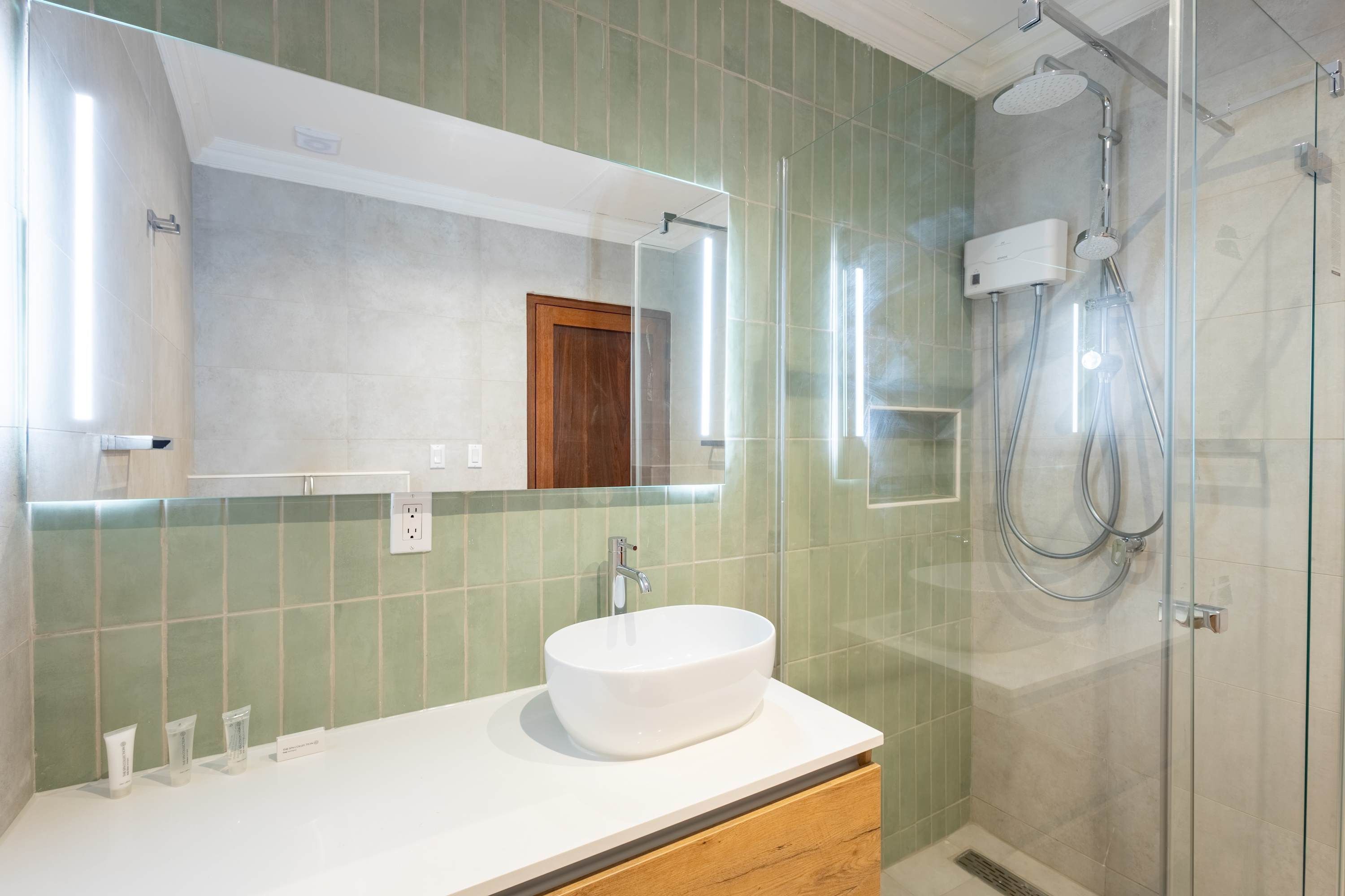 Un baño con un lavabo blanco, un espejo grande y una zona de ducha con mampara de cristal.