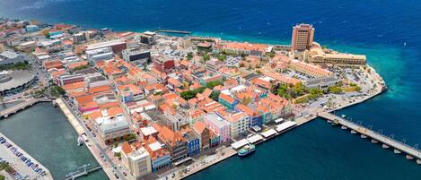 An aerial view of a coastal town with colorful buildings, a marina, and a bridge connecting to the mainland.