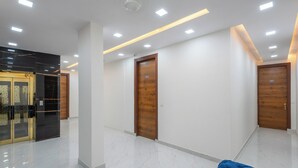 A spacious hallway with white walls, wooden doors, and a blue chair. - Park Pacific By Saavi Hotel (Gurugram)