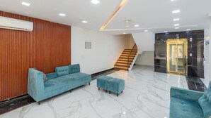 A modern lobby with a blue sofa, matching ottoman, wooden panel wall, and a staircase with illuminated steps. - Park Pacific By Saavi Hotel (Gurugram)