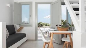 A modern living room with a sofa, a dining table with chairs, and a view of the outdoors through open doors.