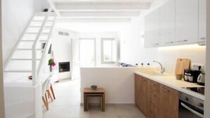 A compact kitchen with white cabinets, a wooden countertop, and a small stool. - White Orchid Suites | 2 | Heated Shared Mini Pool (Vothonas)