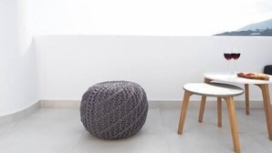 A minimalist room with a round knitted ottoman, a small round table with two chairs, and a glass of red wine. - White Orchid Suites | 2 | Heated Shared Mini Pool (Vothonas)