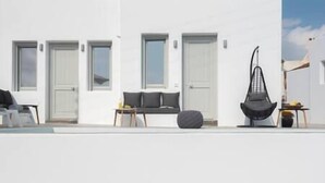 Un edificio moderno de color blanco con diseño minimalista, que incluye un sofá y una silla negra distintiva, una mesita y una planta en maceta.