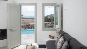 A living room with a sofa, a coffee table, and a view of a pool and beach through open doors. - White Orchid Suites | 6 | Villa | Heated Private Plunge Pool (Vothonas)