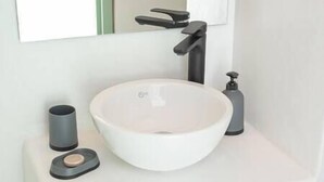 A modern bathroom with a white sink, a black faucet, a soap dispenser, and a small container.
