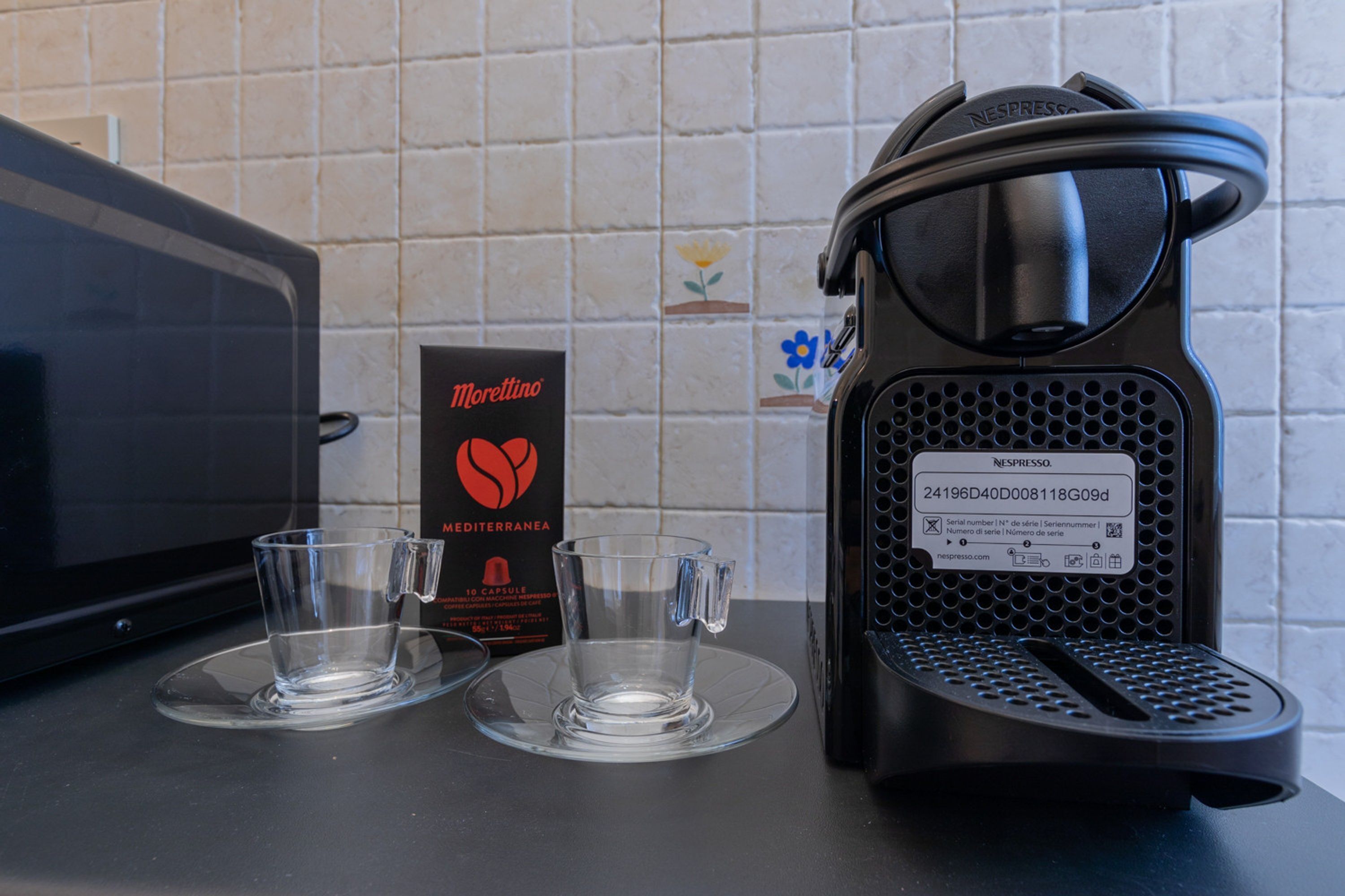 A Nespresso machine, a glass cup, and a Morettino coffee capsule box on a kitchen counter.