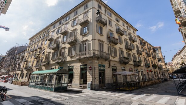 Un edificio de varios pisos con balcones, un café en la planta baja y un paso de peatones.