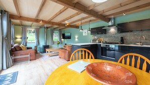 Een gezellig interieur met een houten plafond, een keuken met moderne apparatuur, een eethoek met tafel en stoelen, en een open haard.