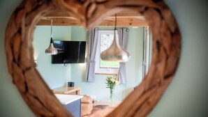 Een hartvormig kijkvenster toont een kamer met een televisie, een raam met gordijnen, een bloevas en een houten tafel.