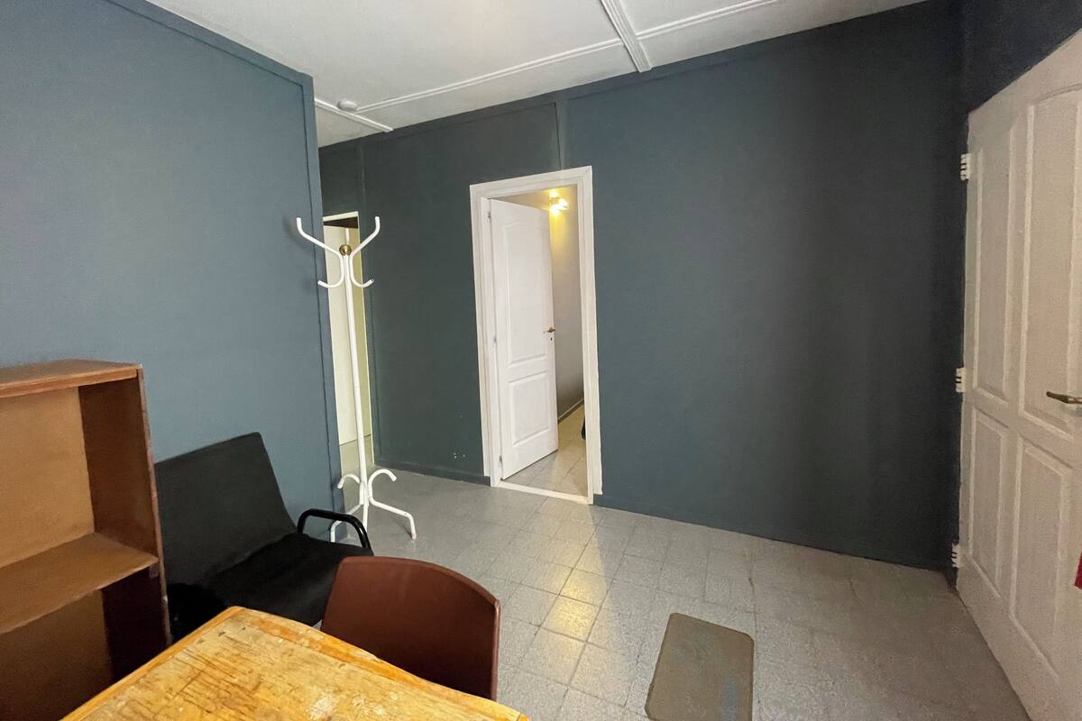A room with a wooden table, a brown chair, a white coat stand, and a door leading to another room.