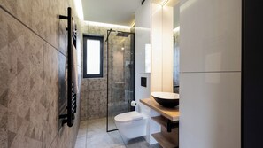 A modern bathroom with a glass shower enclosure, a white toilet, and a wooden vanity with a black basin.