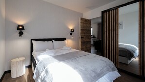 A modern hotel room with a large bed, two wall-mounted lamps, a wooden accent wall, and a mirror reflecting the room.