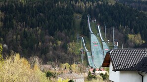 A ski lift with a green track and red and white poles, surrounded by trees and houses. - Sun & Snow Szkolna z widokiem na skocznię (Szczyrk)