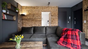 A modern living room with a grey sofa, wooden wall paneling, a wooden coffee table, and a red plaid throw blanket.