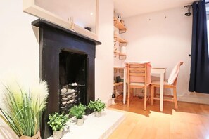 Une pièce avec une cheminée, des chaises en bois, une table à manger et des étagères remplies d’objets.