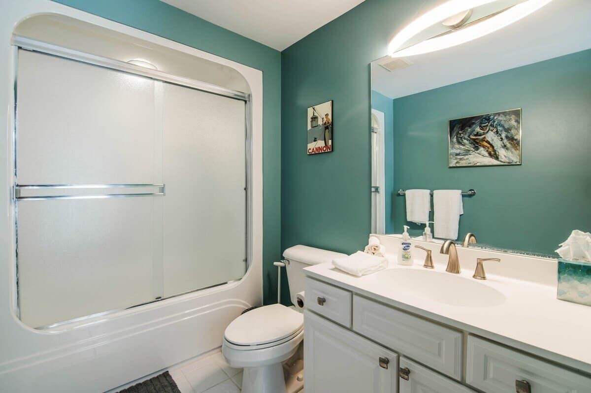 Un baño con bañera, inodoro, lavabo y tocador. Hay dos toallas sobre el lavabo y un cuadro en la pared.