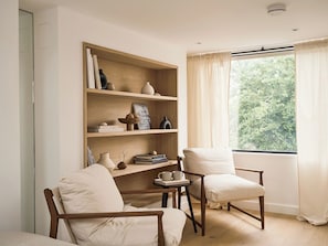 Een kamer met een boekenkast, twee stoelen, een kleine tafel en een raam met gordijnen.