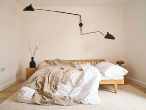 A bedroom with a bed, a bedside table, a lamp, and a vase with branches.