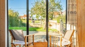 A room with two wooden chairs and a small table, large windows with a view of a garden and a wooden fence. - Plumtrees (4), Thornham, Norfolk (Thornham)