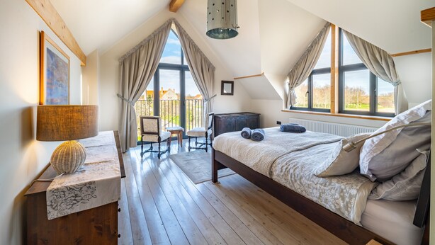 A bedroom with a large bed, wooden floor, a desk with a lamp, and a view of the outside. - Plumtrees (4), Thornham, Norfolk (Thornham)