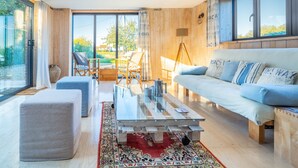 A modern living room with a glass coffee table, a white sofa, and a large window offering a view of the outdoors. - Plumtrees (4), Thornham, Norfolk (Thornham)