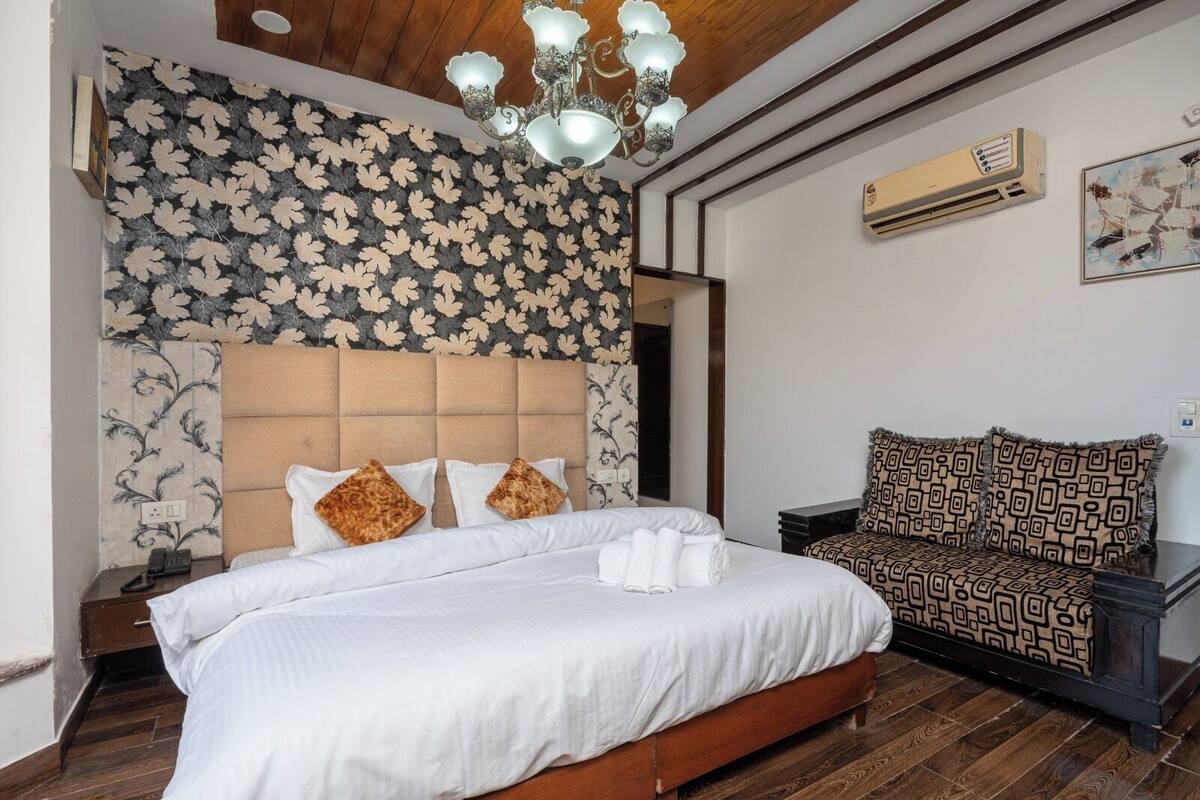 A bedroom with a bed, a sofa, a chandelier, and patterned wallpaper.