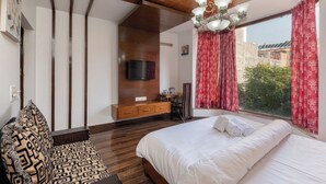 Una camera da letto moderna con un letto grande, soffitto in legno, TV a parete e vista sul verde.