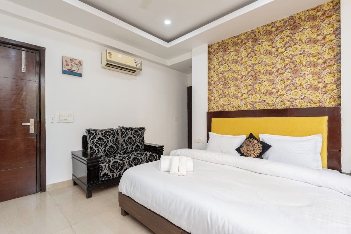 A bedroom with a bed, a nightstand, a chair, an air conditioning unit, and a wall with a floral pattern.