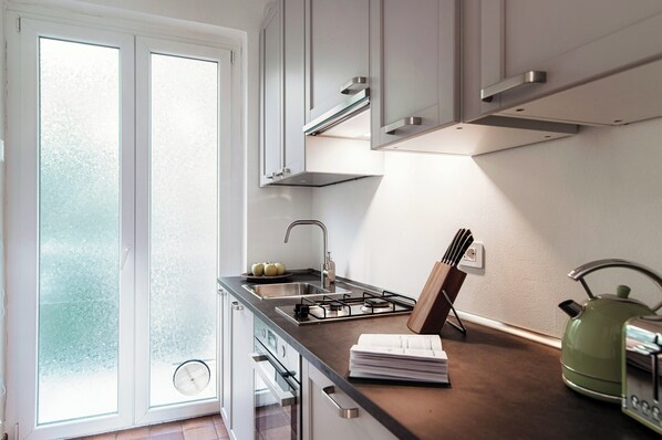 A modern kitchen with a gas stove, sink, and a window with frosted glass. - Horizon (Como)