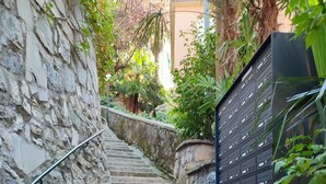 Eine Steintreppe führt zu einem Gebäude, umgeben von Grünpflanzen und einem Metallzaun.