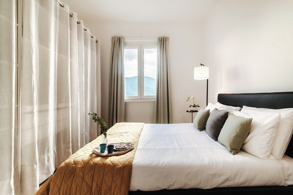 Ein Hotelzimmer mit Bett, Nachttisch mit Frühstücksutensilien, Fenster mit Vorhängen und einer Lampe.