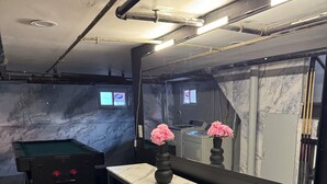 A pool table with a marble top, two black bar stools, a white marble-topped table with a vase of pink flowers, and a large mirror reflecting the room. - Pleasant 3-bedroom home in East Orange, NJ located close to the train stations. (East Orange)