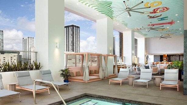 A modern indoor pool area with lounge chairs, a pool, and a bar area with seating.