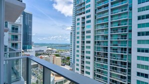 A high-rise building with multiple balconies and large windows, overlooking a coastal area with a bridge in the distance.