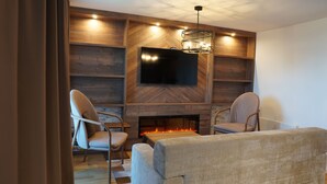 A modern living room with a fireplace, two armchairs, a sofa, and a flat-screen TV mounted on a wooden wall.