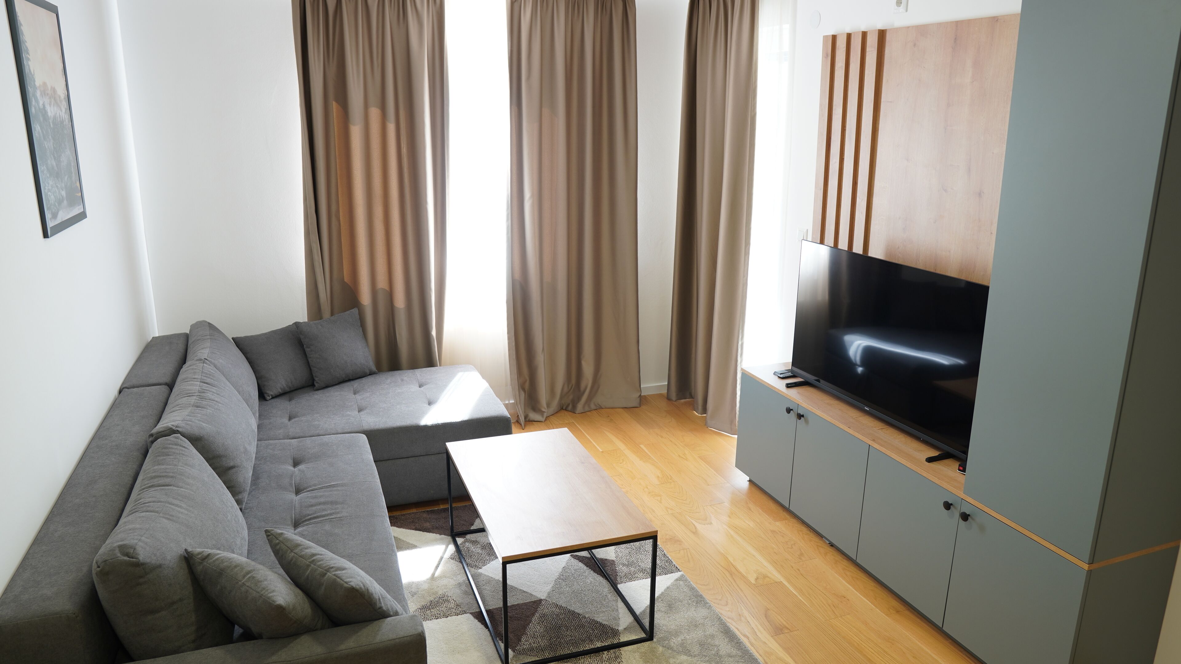 A modern living room with a grey sofa, a coffee table, and a flat-screen TV on a wooden cabinet.