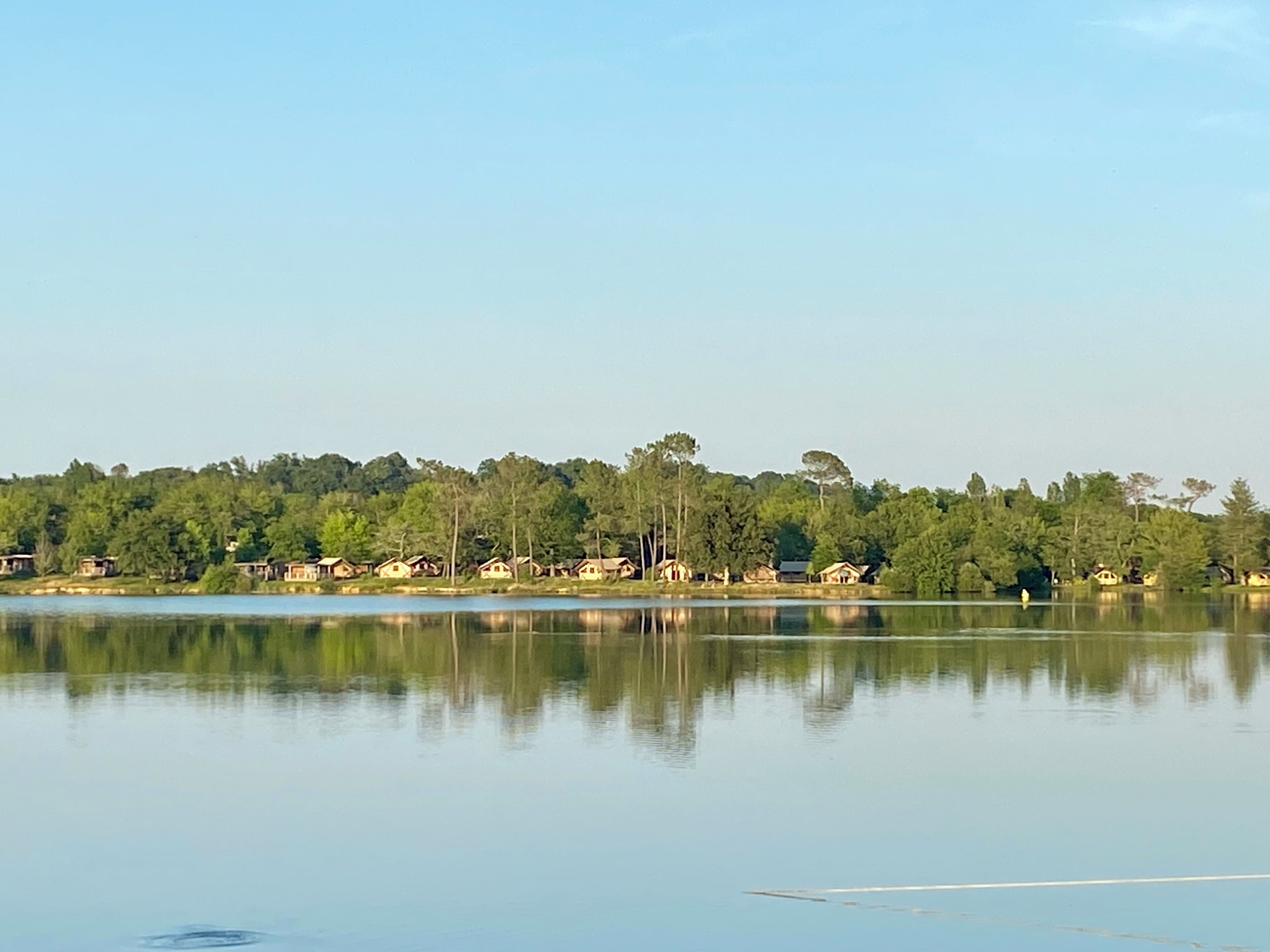 A calm lake with a forested shoreline and several small cabins.