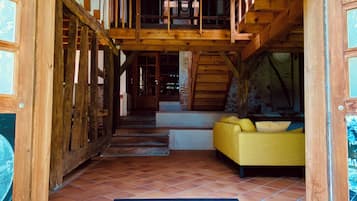 Un intérieur en bois avec un escalier menant à un niveau supérieur, un canapé jaune et un paillasson noir sur un sol carrelé.