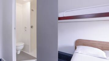 Un baño con inodoro y ducha, y una cama con cabecera de madera y ropa de cama blanca.