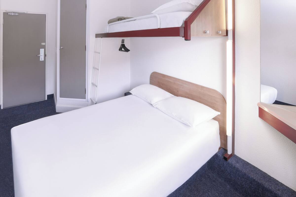 A single bed with a wooden headboard, a small bedside table, and a white mattress.