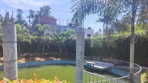 A circular water feature with a metal railing, surrounded by lush greenery and palm trees. - Secret Paradise Sylhet (Sylhet)