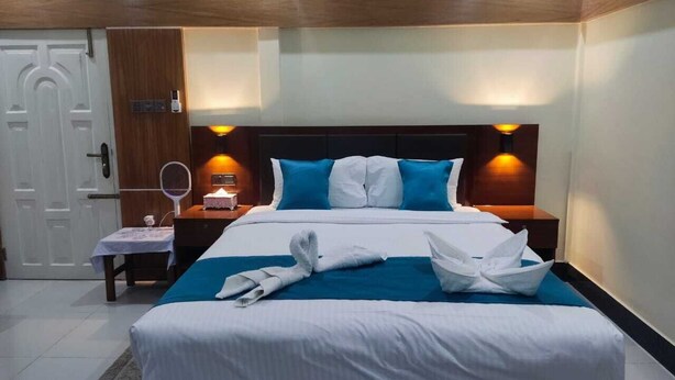 A hotel room with a large bed, two bedside tables, a nightstand, a mirror, and a door. - Secret Paradise Sylhet (Sylhet)