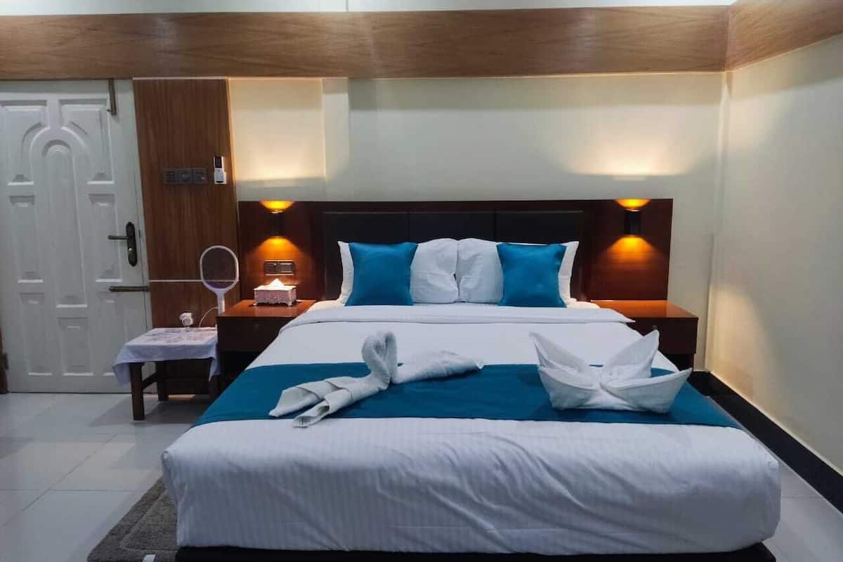A hotel room with a large bed, two bedside tables, a nightstand, a mirror, and a door.