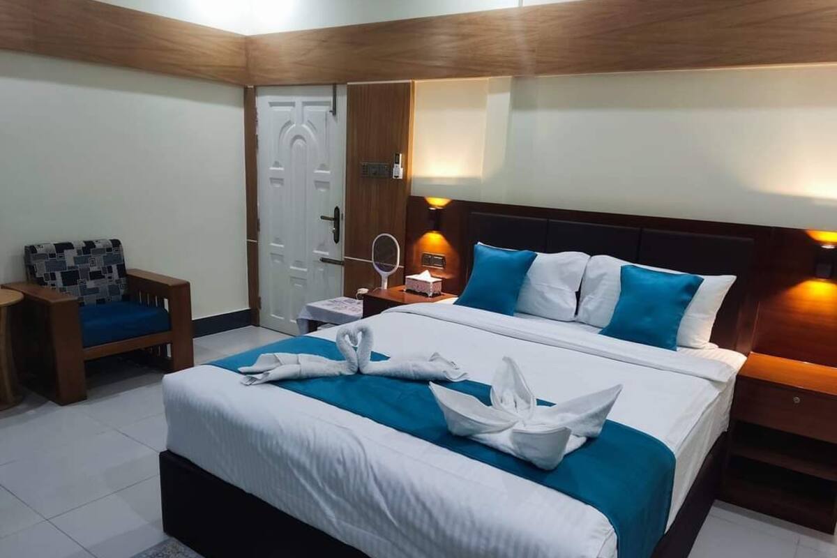 A neatly arranged hotel room with a large bed, a bedside table with a lamp, a chair, and a door.