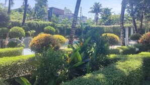 A well-maintained garden with various shrubs and palm trees, a white gate, and a building in the background. - Secret Paradise Sylhet (Sylhet)