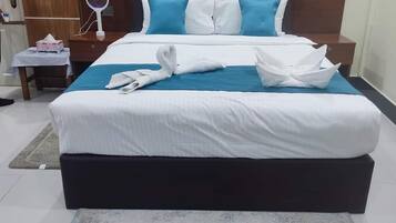 Quarto de hotel com uma cama, um guarda-roupa de madeira, uma mesa de cabeceira com abajur e um tapete azul estampado.