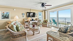 A spacious living room with wicker furniture, a ceiling fan, a flat-screen TV, and a large sliding glass door leading to a balcony with a view of the ocean. - 3BR/3BA Close to Main St-Oceanfront-Tidemaster 301 (North Myrtle Beach)