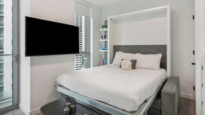 Ein modernes Hotelzimmer mit einem Bett, einem an der Wand befestigten Fernseher, einem kleinen Tisch und einer Bank.